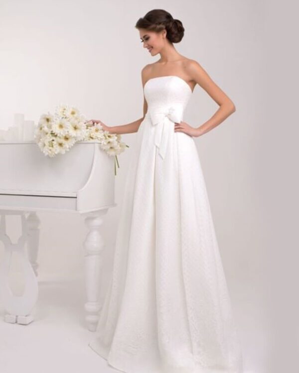 Στράπλες  νυφικό σε Άλφα γραμμή με υπέροχο δέσιμο στη μέση με πλούσιο φιόγκο. Σε ανάγλυφο γαλλικό σατέν. Υπέροχο δέσιμο με κορδέλα στην πλάτη σε στυλ κορσέ.