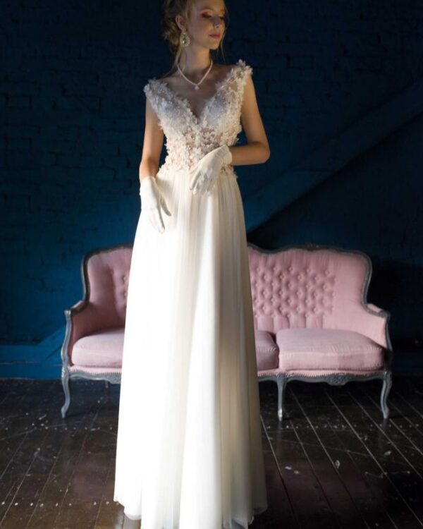 Μεταξωτό νυφικό σε ίσια γραμμή , με φούστα από μεταξωτή μουσελίνα. Με υπέροχο ολοκέντητο μπούστο με 3D μεταξωτά χειροποίητα λουλούδια, που καταλήγει σε βαθύ V στην πλάτη και το μπούστο. Αέρινη γραμμή. Ελληνικής ραφής