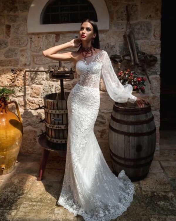 Γοργονέ νυφικό ολοκέντητο  με γαλλική δαντέλα και διαφάνεια soleil στο μπούστο, με έναν ώμο και φουσκωτό μανίκι δαντέλα. Φούστα γοργόνας με μακριά ουρά.