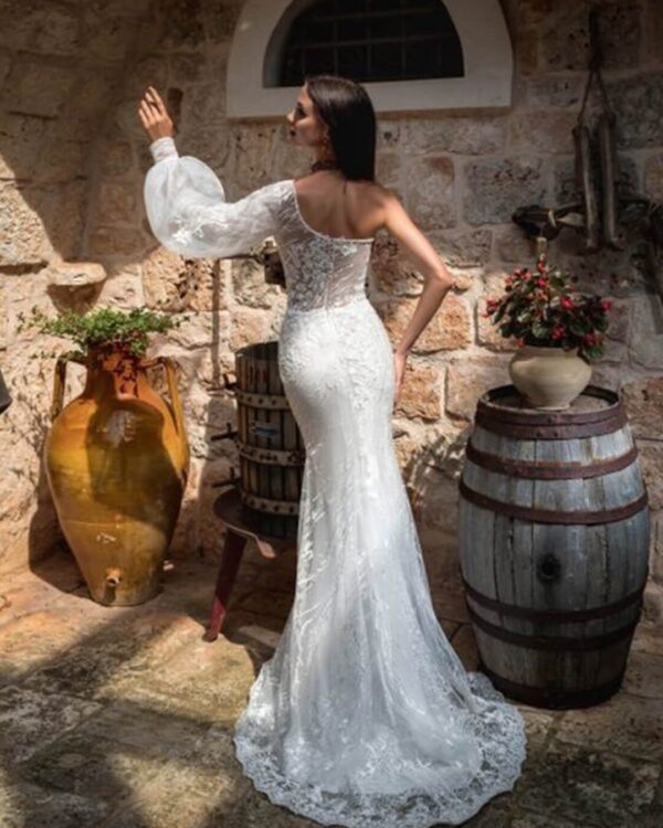 Γοργονέ νυφικό ολοκέντητο  με γαλλική δαντέλα και διαφάνεια soleil στο μπούστο, με έναν ώμο και φουσκωτό μανίκι δαντέλα. Φούστα γοργόνας με μακριά ουρά.