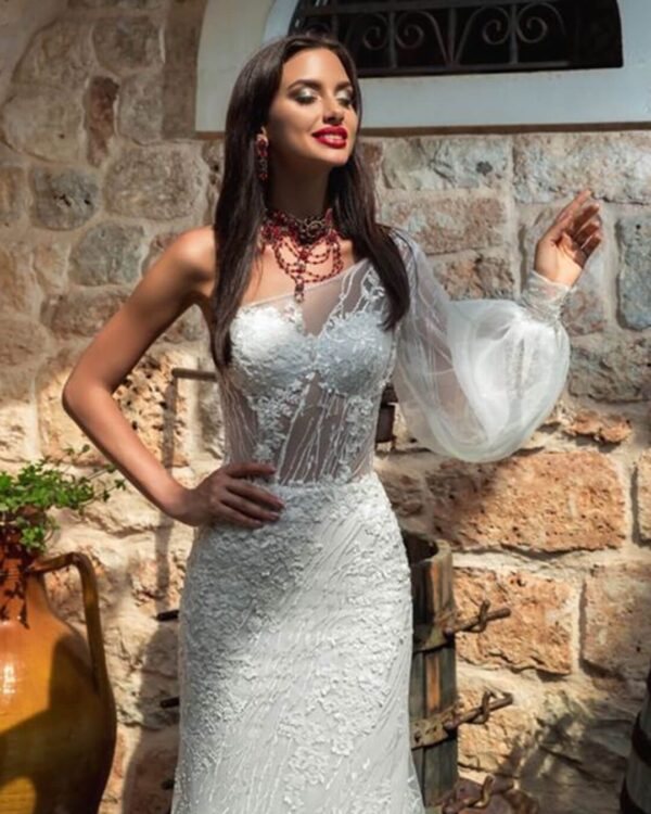 Γοργονέ νυφικό ολοκέντητο  με γαλλική δαντέλα και διαφάνεια soleil στο μπούστο, με έναν ώμο και φουσκωτό μανίκι δαντέλα. Φούστα γοργόνας με μακριά ουρά.