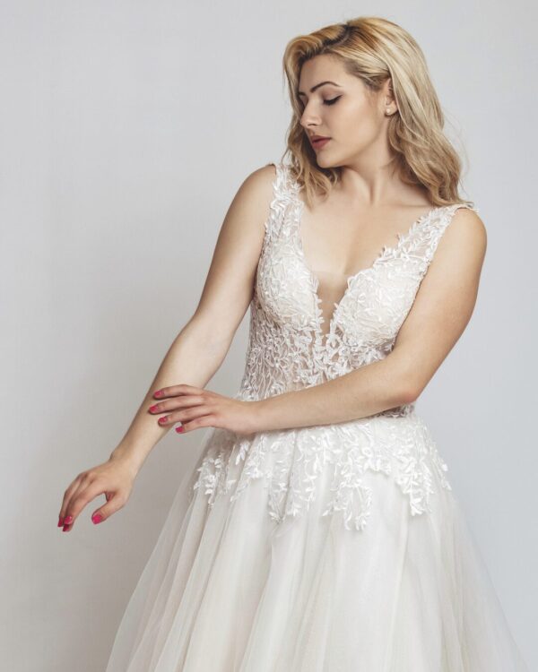 Εντυπωσιακό νυφικό με διαφάνεια στο μπούστο και κεντημένο με ανάγλυφη γαλλική δαντέλα. Φούστα σε άλφα γραμμή, από γαλλικό τούλι σε λευκό με νερά στο χρώμα της πούδρας. Ανοιχτή πλάτη σε βαθύ V. 