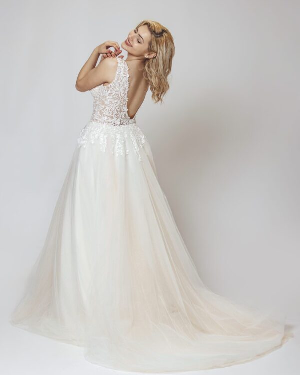 Εντυπωσιακό νυφικό με διαφάνεια στο μπούστο και κεντημένο με ανάγλυφη γαλλική δαντέλα. Φούστα σε άλφα γραμμή, από γαλλικό τούλι σε λευκό με νερά στο χρώμα της πούδρας. Ανοιχτή πλάτη σε βαθύ V. 