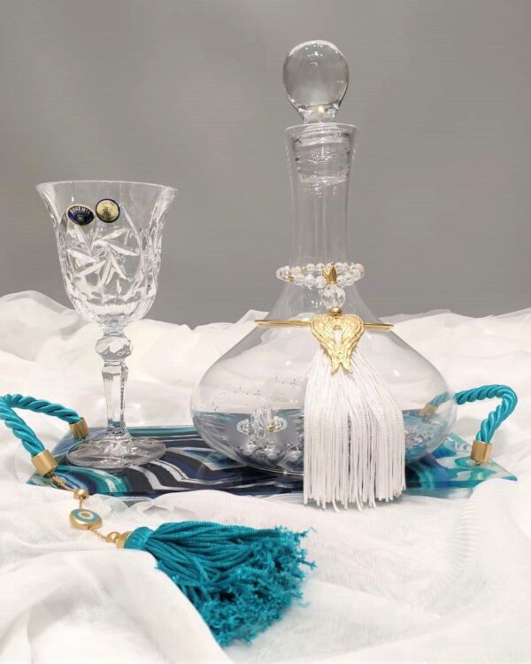 Σετ κουμπάρου σε κρύσταλλο Βοημίας με επίχρυσο στολισμό Tresento. Το σετ περιλαμβάνει περίτεχνο δίσκο με σμάλτο και πλεξιγκλάς, ιδιαίτερη μποτίλια κρασιού και ποτήρι από κρύσταλλο Βοημίας, διακοσμημένο με επιχρυσωμένο 24 καρατίων στολίδι Tresento με φτερά αγγέλου, με πέταλο, γαλάζια φούντα και μεταξωτό κορδόνι. Όλα είναι χειροποίητα και κατασκευασμένα στην Ελλάδα.