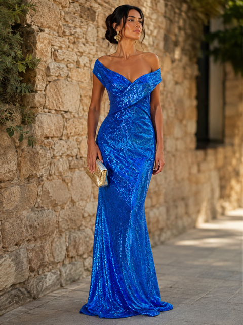 Woman in a blue off-shoulder sequin gown standing against a stone wall, holding a gold clutch.