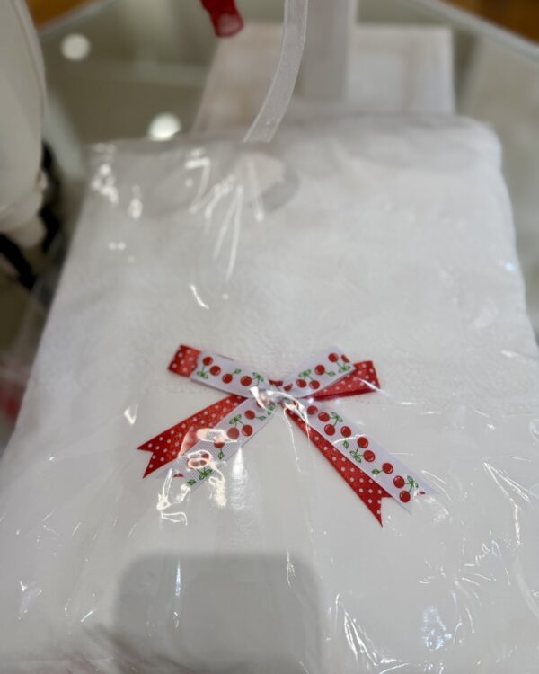 White gift package wrapped in clear plastic with a red-and-white cherry-pattern bow on top.