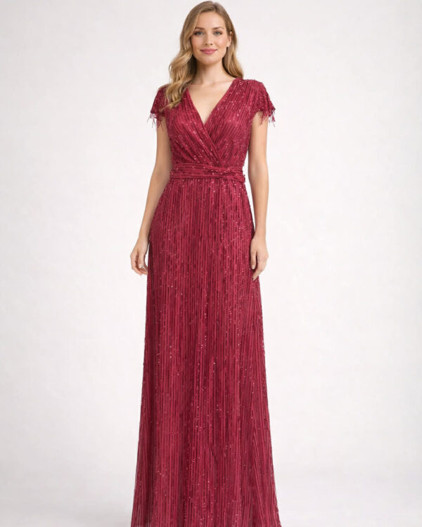 Woman wearing a floor-length burgundy evening gown with a wrapped waist and fringed cap sleeves, posing for a fashion shoot (MissVanity.gr)