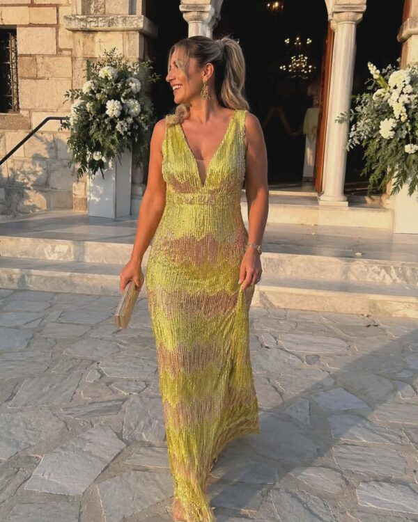 Woman in a lime-green, sequin evening gown with a plunging neckline standing on stone steps outside a building, holding a clutch and smiling.