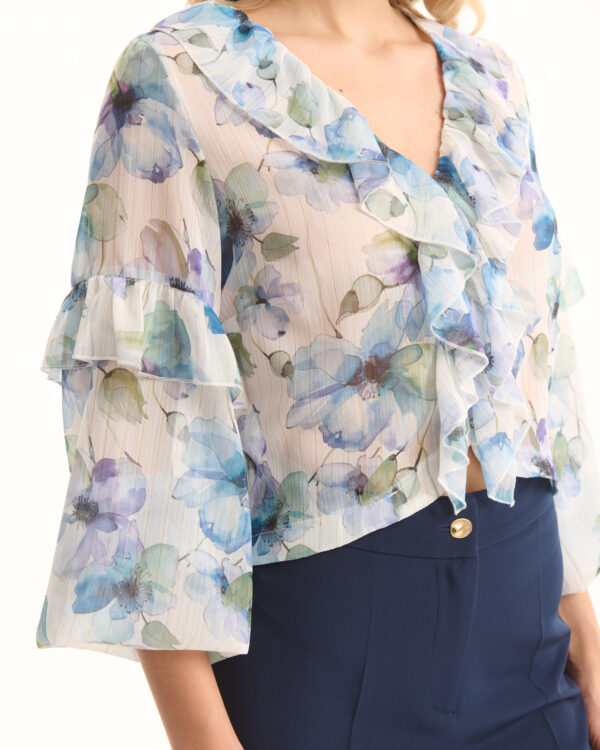 Woman wearing a sheer floral blouse with ruffles over navy high-waisted pants, close-up of torso and shoulders.