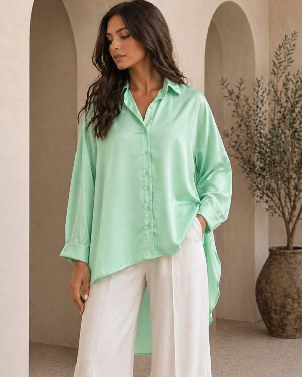 Woman in a mint-green button-down blouse and white wide-leg pants stands in a beige architectural interior with arches.