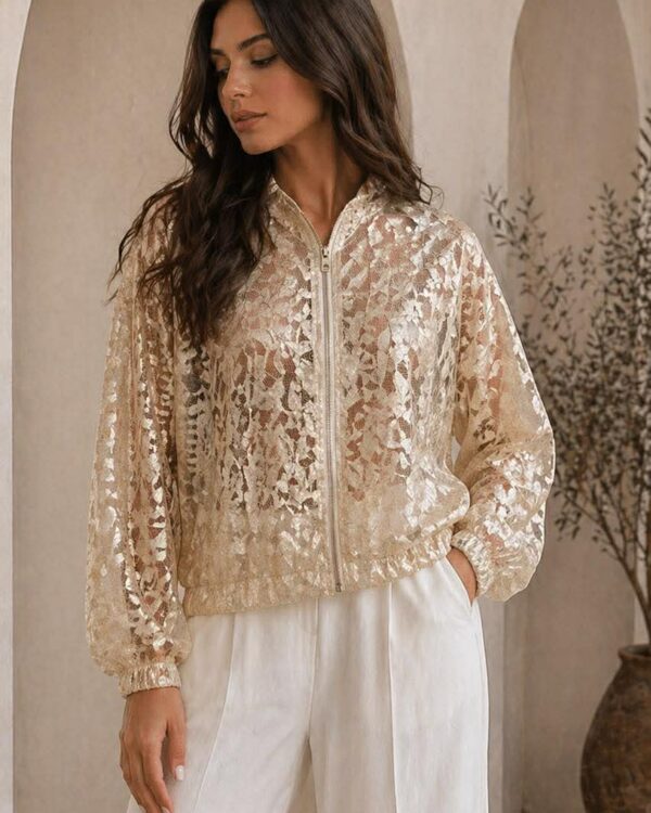 Woman in a cream lace zip-up jacket and white wide-leg pants, standing indoors with 'missvanity.gr' logo in the background.