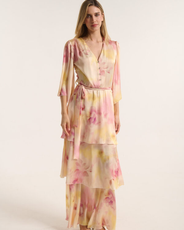 Full-body portrait of a woman in a pastel pink-yellow floral dress with a tie waist, standing against a light studio backdrop.