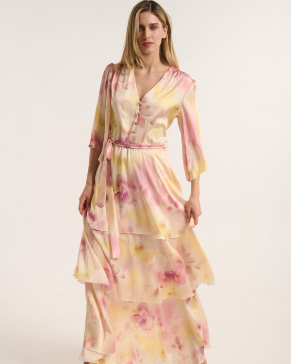 Woman in a pastel pink and yellow floral dress, standing against a light neutral backdrop, posing confidently.