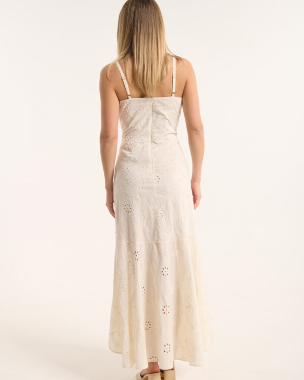 Back view of a woman in a cream floral lace maxi dress, standing with beige sandals on a light background.