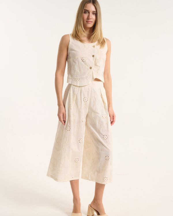 Model wearing a cream sleeveless embroidered top and matching wide-leg pants with floral cut-outs, standing against a light backdrop.
