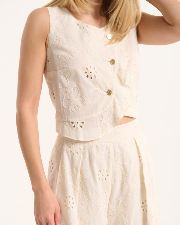 Woman wearing a cream lace dress with large floral embroidery and gold buttons, shown from the chest down to the hip area.