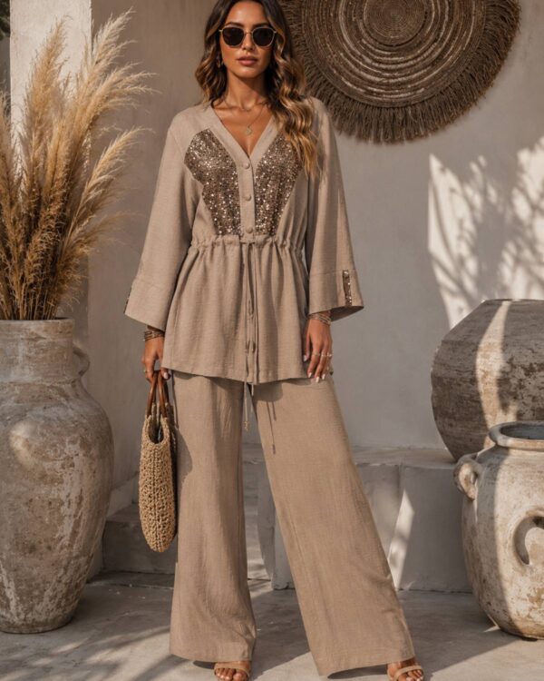 Woman wearing a beige sequined top with matching wide-leg pants, holding a woven bag, and sunglasses, standing outdoors.