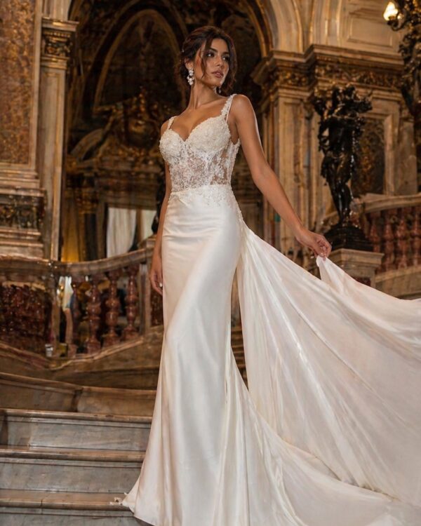Bride in ivory lace wedding gown with a long train posing on a marble staircase in a grand, ornate hall.
