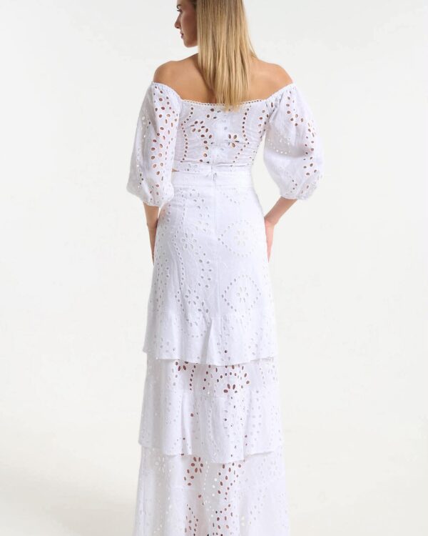 Back view of a woman in a white off-the-shoulder eyelet dress with puff sleeves and a tiered skirt.