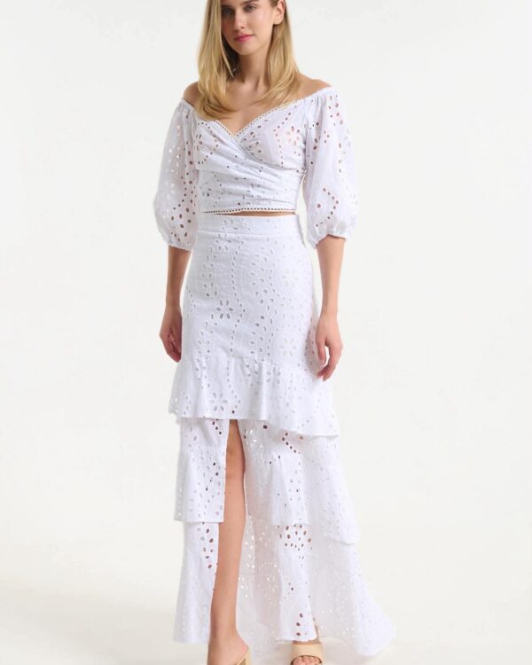 Woman in a white off-shoulder eyelet top and tiered maxi skirt with floral cutouts, facing forward.