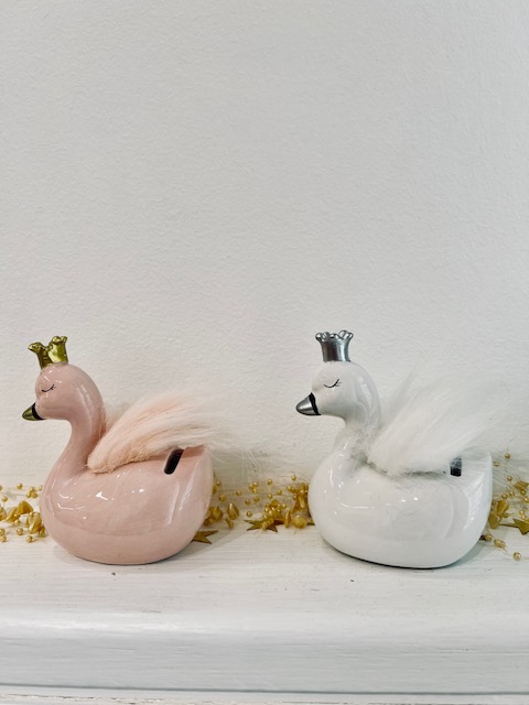 Two ceramic swan figurines, pink and white, with fluffy tails and small crowns on a white shelf with yellow petals nearby.