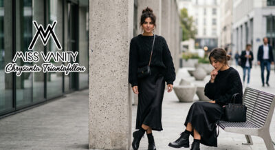 Urban fashion scene: two women in black outfits on a city sidewalk, one standing by a concrete pillar with a crossbody bag, the other seated with a black handbag; Miss Vanity logo on the left.