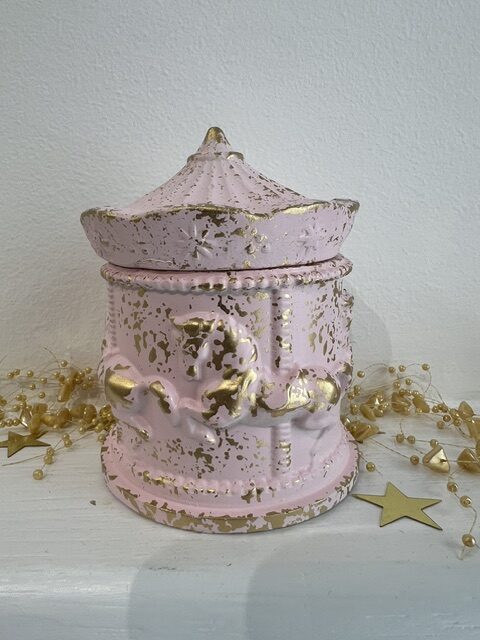 Distressed pink ceramic trinket box with a lid and gold accents on a white surface with gold bead garlands and star shapes.