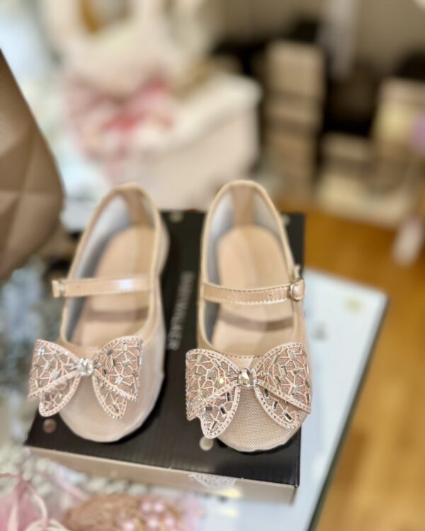 Beige Mary Jane–style children’s shoes with jeweled bows on display in a store