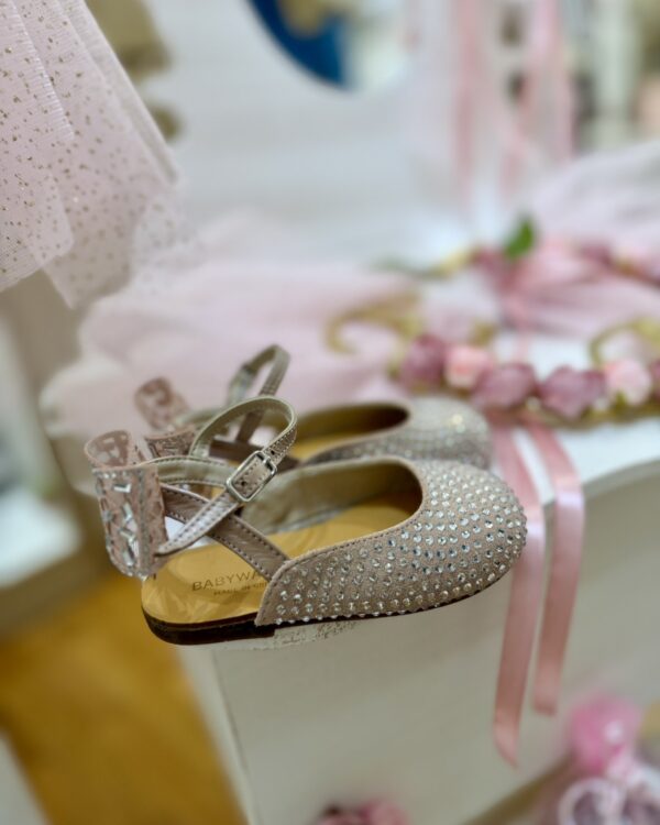 Beige glitter baby shoe with a small buckle, displayed among pastel pink decorations.