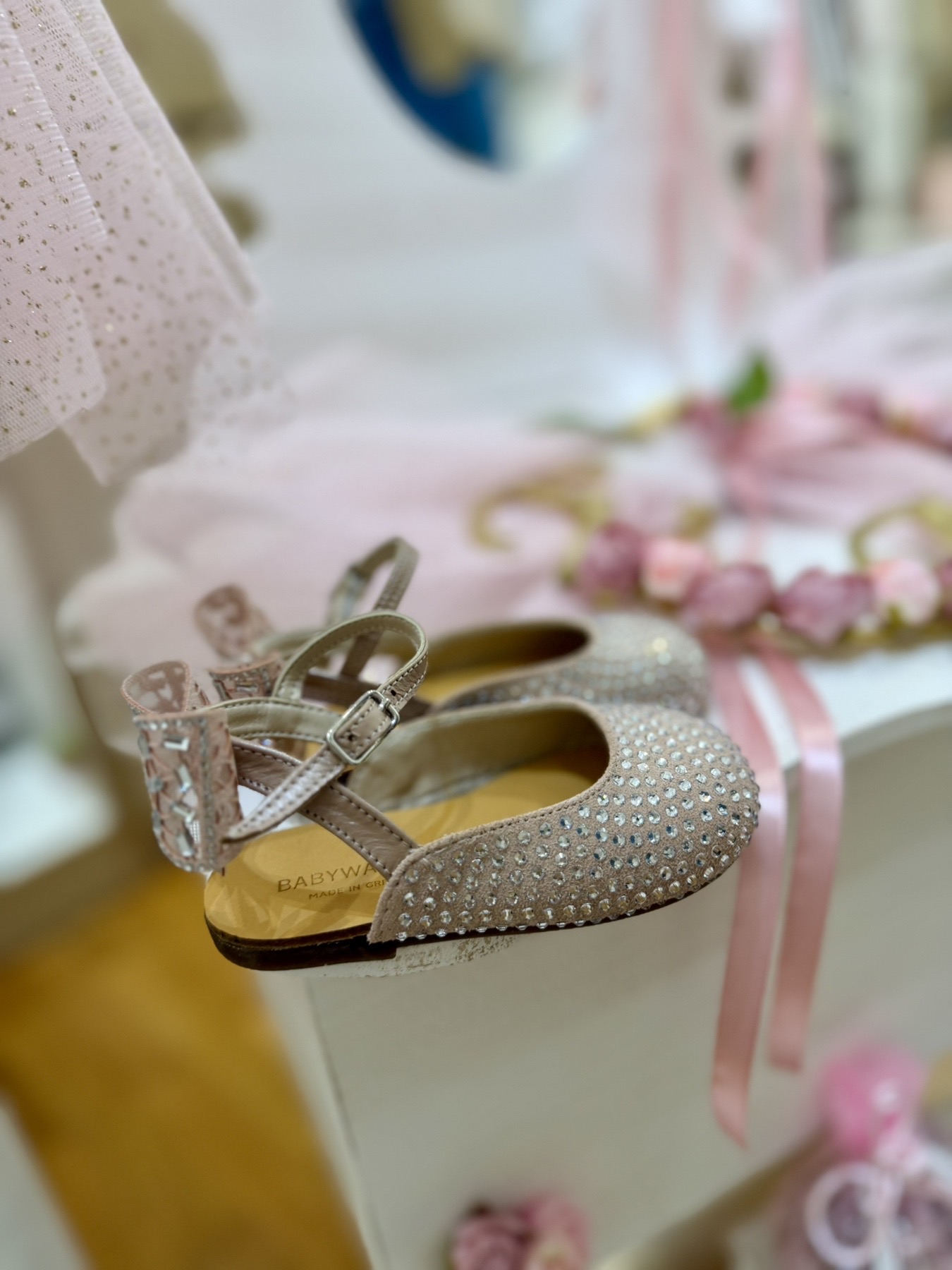 oloklhrwmeno paketo baptishs me ksulino mpoudouar(2) Beige glitter baby shoe with a small buckle, displayed among pastel pink decorations.
