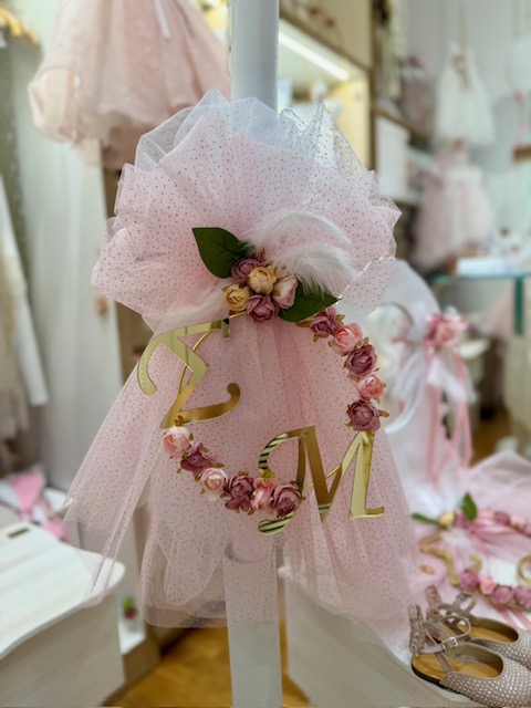 oloklhrwmeno paketo baptishs me ksulino mpoudouar(5) Pink tulle dress decoration on a stand, adorned with a flower wreath and gold initials in a boutique display.