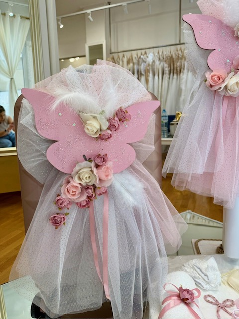 Pink butterfly-themed dress display on a mannequin, featuring a tulle skirt and rose garland in a boutique window.
