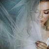 Woman with a sheer veil draped over her face, eyes closed, makeup visible, soft lighting (bridal portrait)