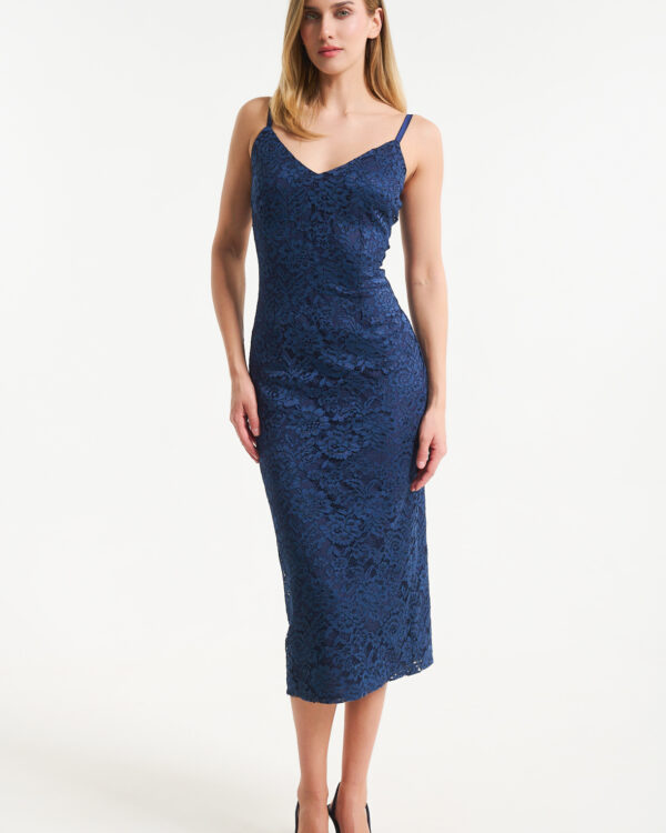Woman in a navy blue lace midi dress with thin straps standing against a light background, wearing matching navy heels.