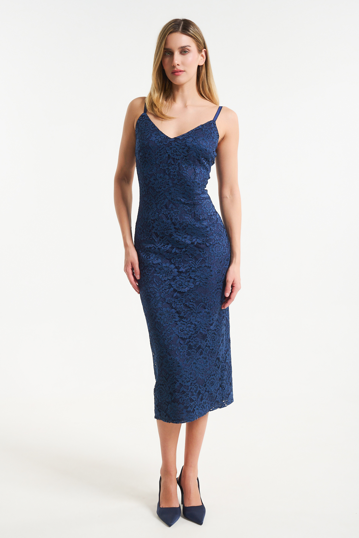 romantic midi forema me dantela kai leptes tirantes(2) Woman in a navy blue lace midi dress with thin straps standing against a light background, wearing matching navy heels.