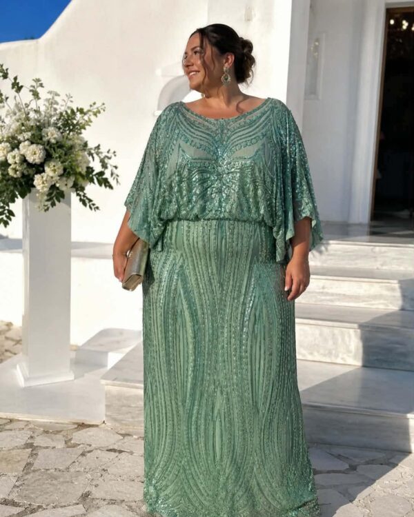 Woman in a mint-green, beaded gown posing outdoors beside white architecture and a flower arrangement, smiling and wearing statement earrings and a clutch