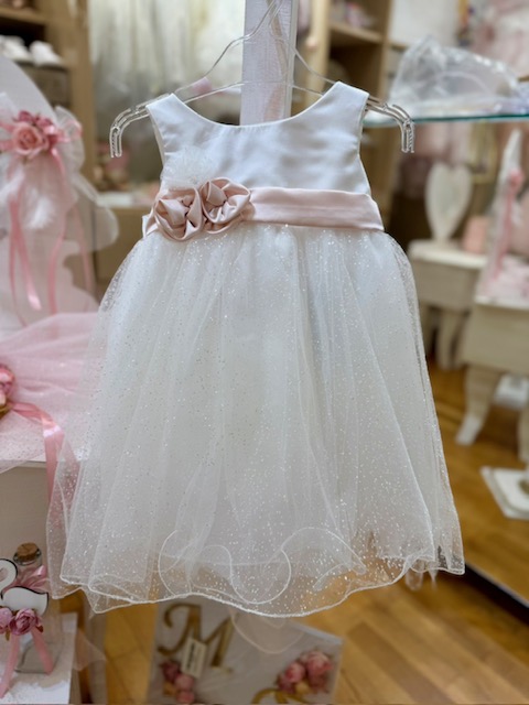 oloklhrwmeno paketo baptishs me ksulino mpoudouar(7) White sleeveless toddler dress with a pale pink sash and fabric flower, sparkly tulle skirt, hanging on a hanger in a boutique.