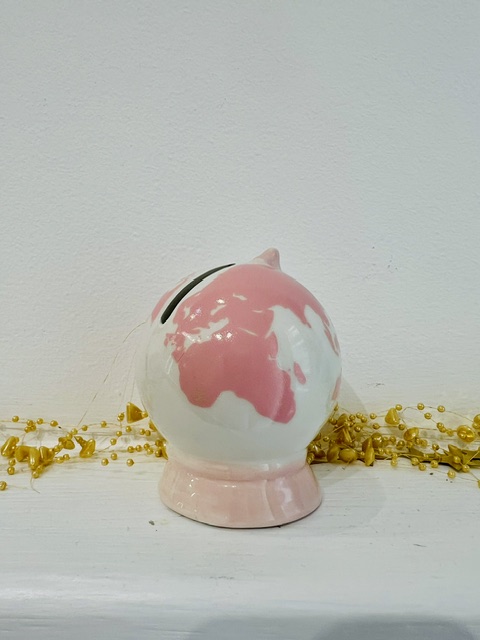Globe-themed piggy bank with a pink-and-white world map design, sitting on a pink stand with coins scattered around.