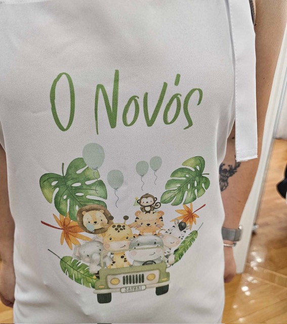 White apron with green 'O Novos' text and a cartoon safari jeep with smiling animals among tropical plants.