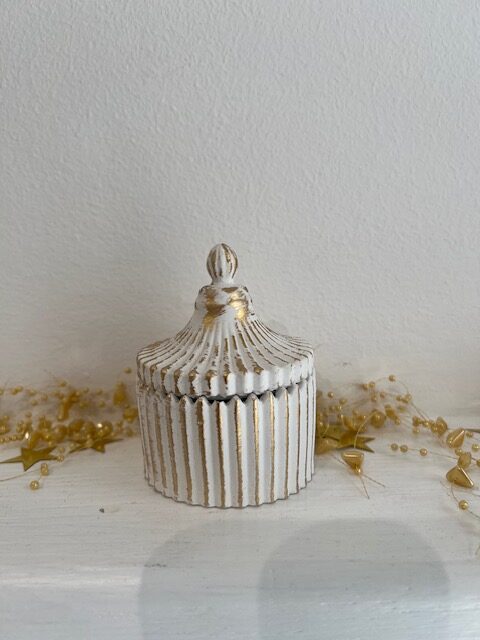White ribbed decorative jar with gold accents and a knobbed lid, sitting on a white surface with scattered gold beads.