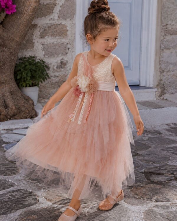 Little girl in a peach tutu dress with a flower sash, walking on a stone path outdoors.