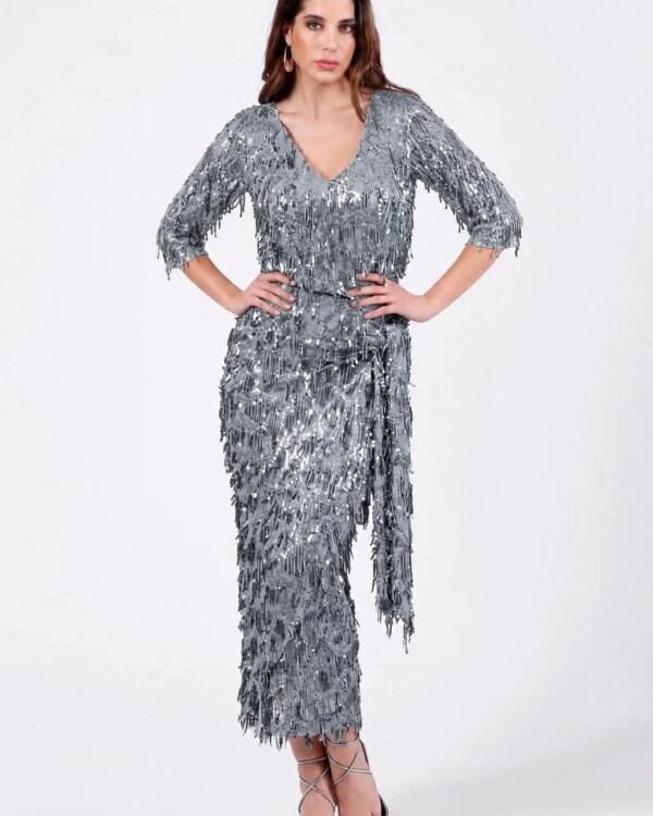Woman in a silver sequin fringe dress with a V-neck, hands on hips, wearing strappy heels.