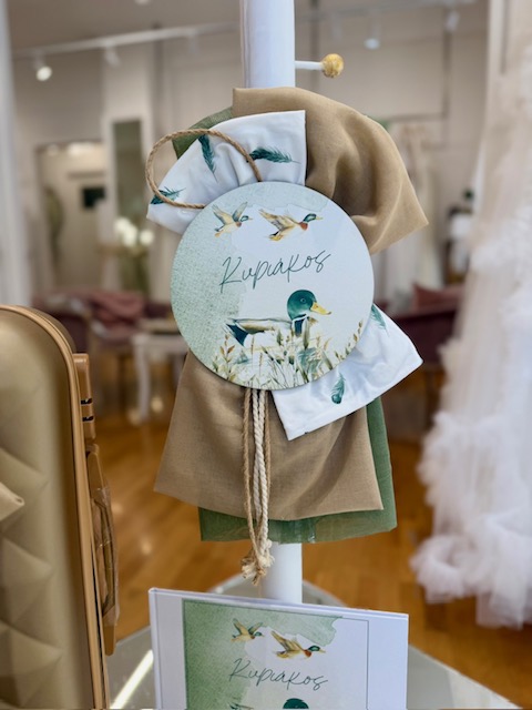 oloklhrwmeno paketo baptishs me thema th xhna (5) Decorative fabric display on a white stand featuring a round tag with duck illustrations and the word 'Kupakos', tied with rope.