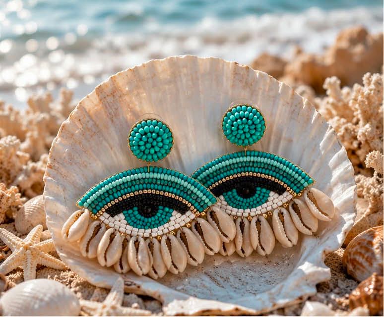 xeiropoihta skoularikia mati me xantres kai koxulia(2) Turquoise beaded earrings shaped like eyes resting in a seashell on a sunny beach.