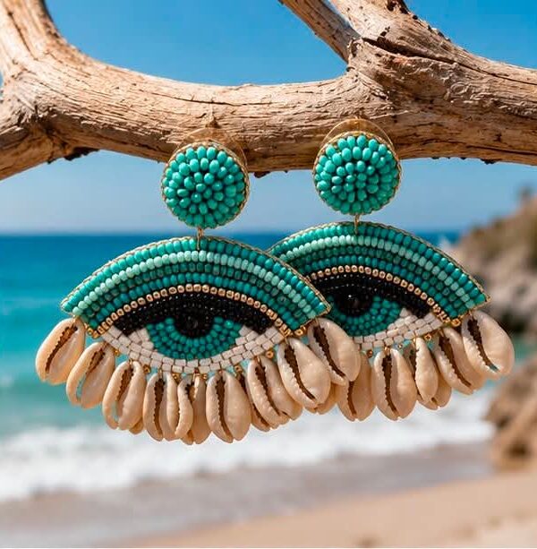 Turquoise beaded earrings shaped like eyes hang from a weathered branch at the beach.