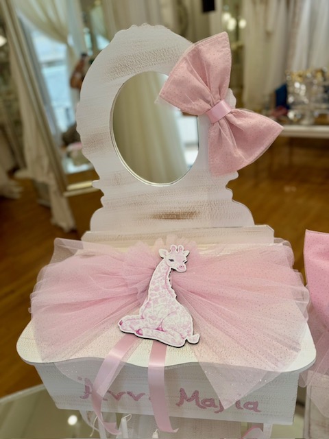 oloklhrwmeno paketo baptishs me ksulino mpoudouar me thema thn kamhlopardalh(3) White decorative vanity stand with an oval mirror, pink tulle drape, a large pink bow, and a pink giraffe figurine on a gift-box style base.