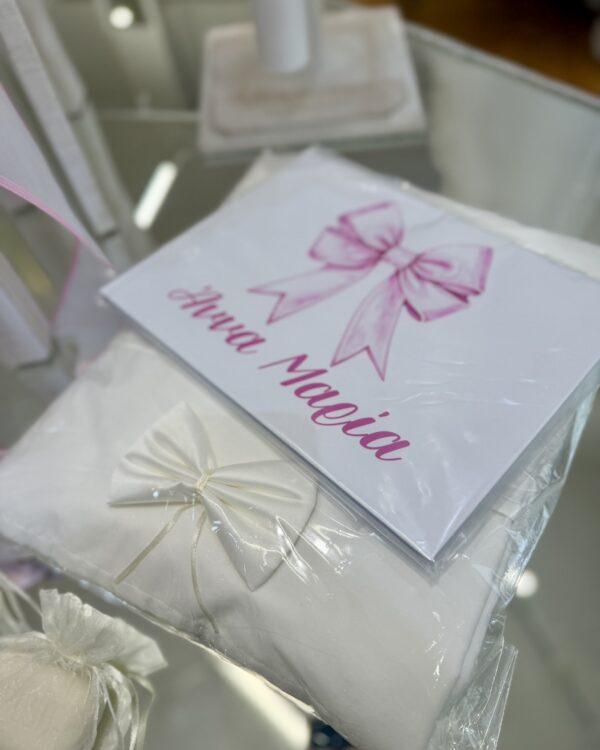 White gift box wrapped in white paper with a pink ribbon bow, among other wrapped presents.