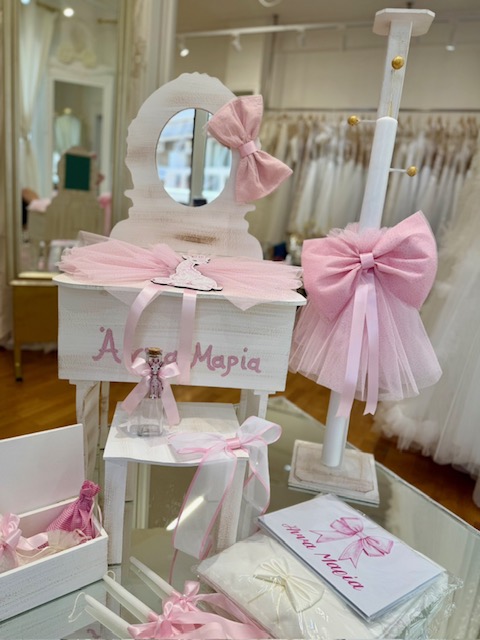 White wooden display vanity with a round mirror, pink bows and tulle, and matching gift boxes in a bridal shop window or boutique.
