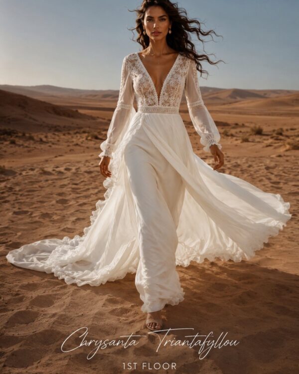 Bride wearing a flowing white lace wedding dress walks across a desert landscape at sunset.